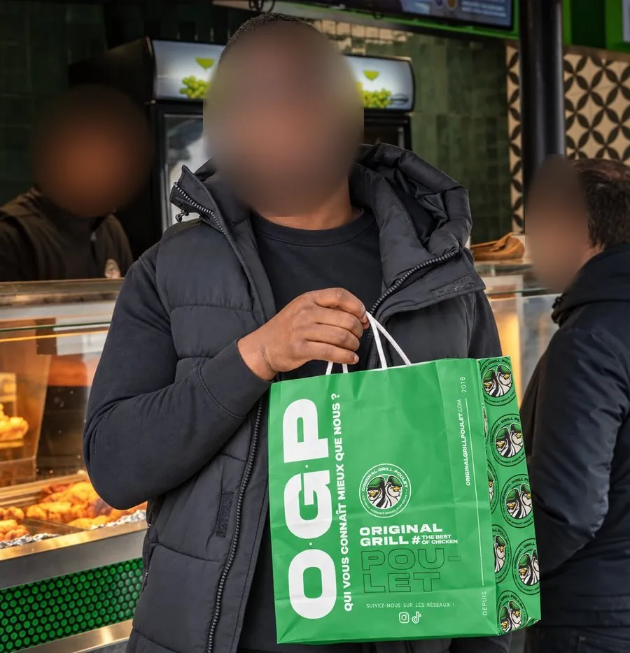 Client tenant le sac à emporter vert Original Grill Poulet au comptoir